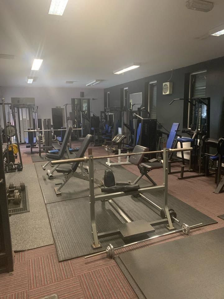 The main gym floor, lined with resistance machines, benches, an Olympic bar and dumbbells.