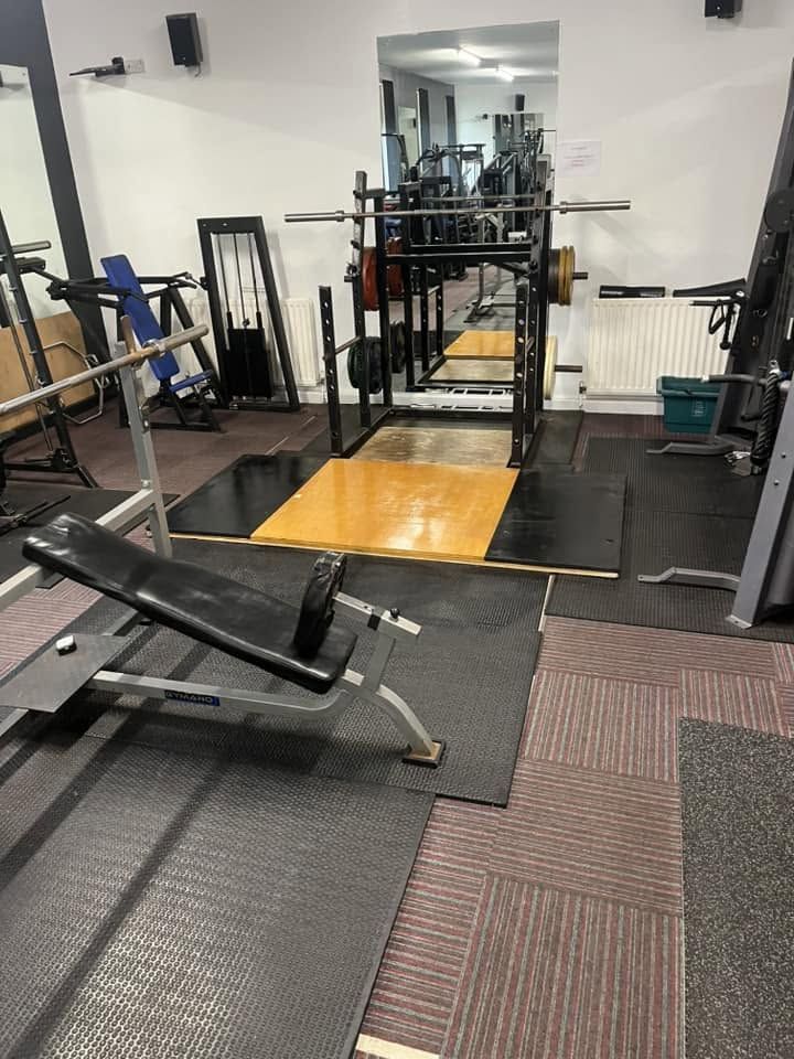 Squat rack set over a wooden lifting platform, with an adjustable bench, weight plates and full-length mirrors.